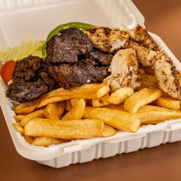 A takeout container filled with golden french fries, grilled chicken, and dark beef, with lettuce and tomato.