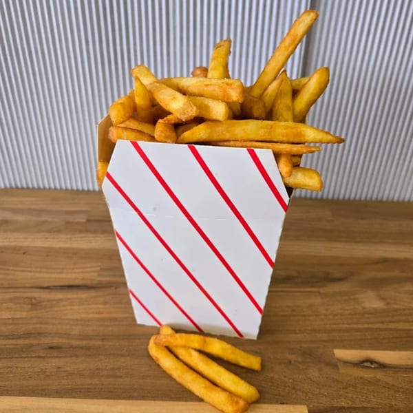 A white paper container with red stripes overflowing with golden french fries on a wooden table.