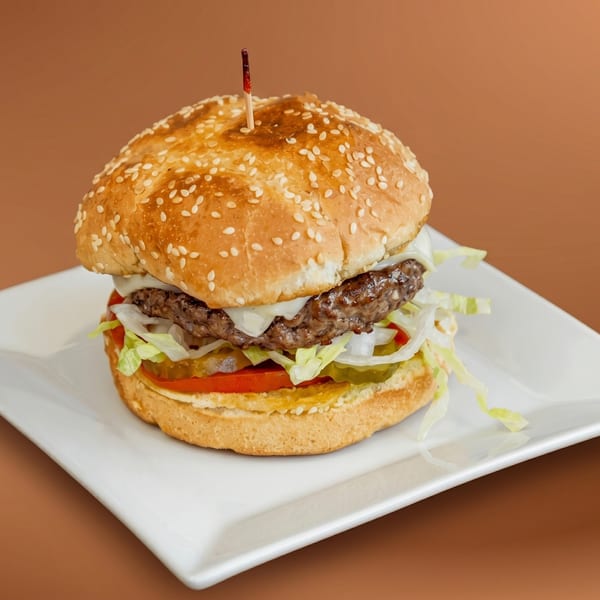 A juicy cheeseburger with lettuce, tomato, onions, and pickles on a sesame seed bun.