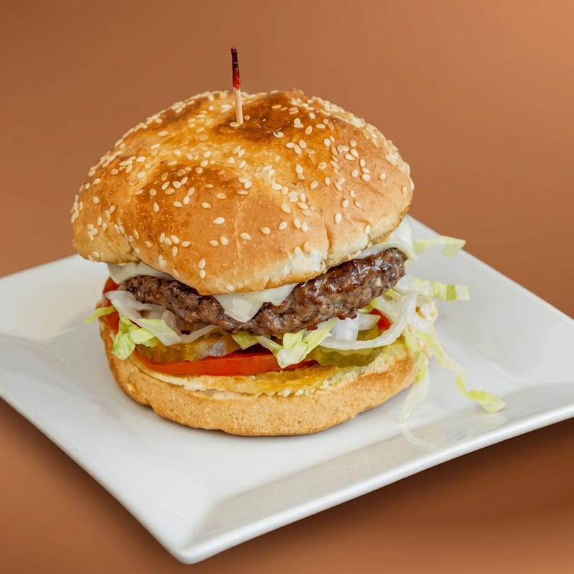 A juicy cheeseburger with lettuce, tomato, onions, and pickles on a sesame seed bun.