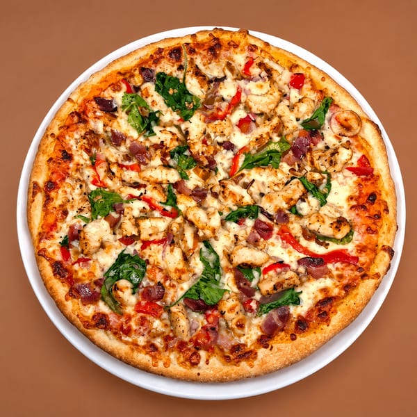 A whole chicken pizza with red peppers, spinach, and red onions on a white plate.