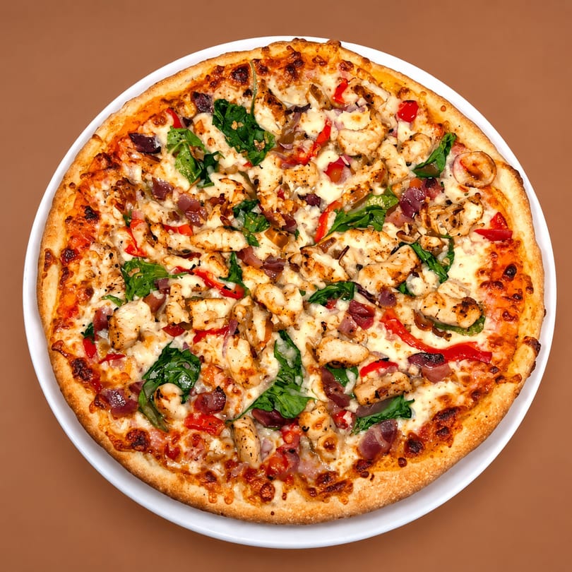 A whole chicken pizza with red peppers, spinach, and red onions on a white plate.
