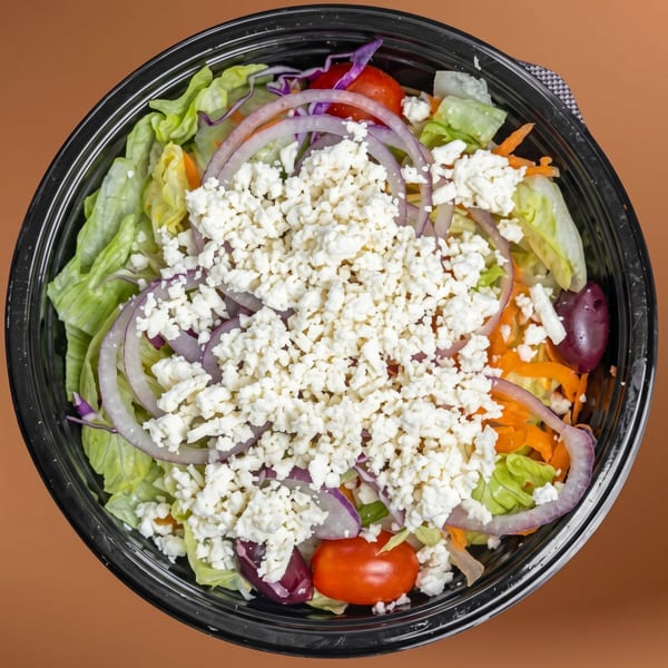 Overhead view of a fresh Greek salad with lettuce, red onions, tomatoes, olives, and feta cheese.