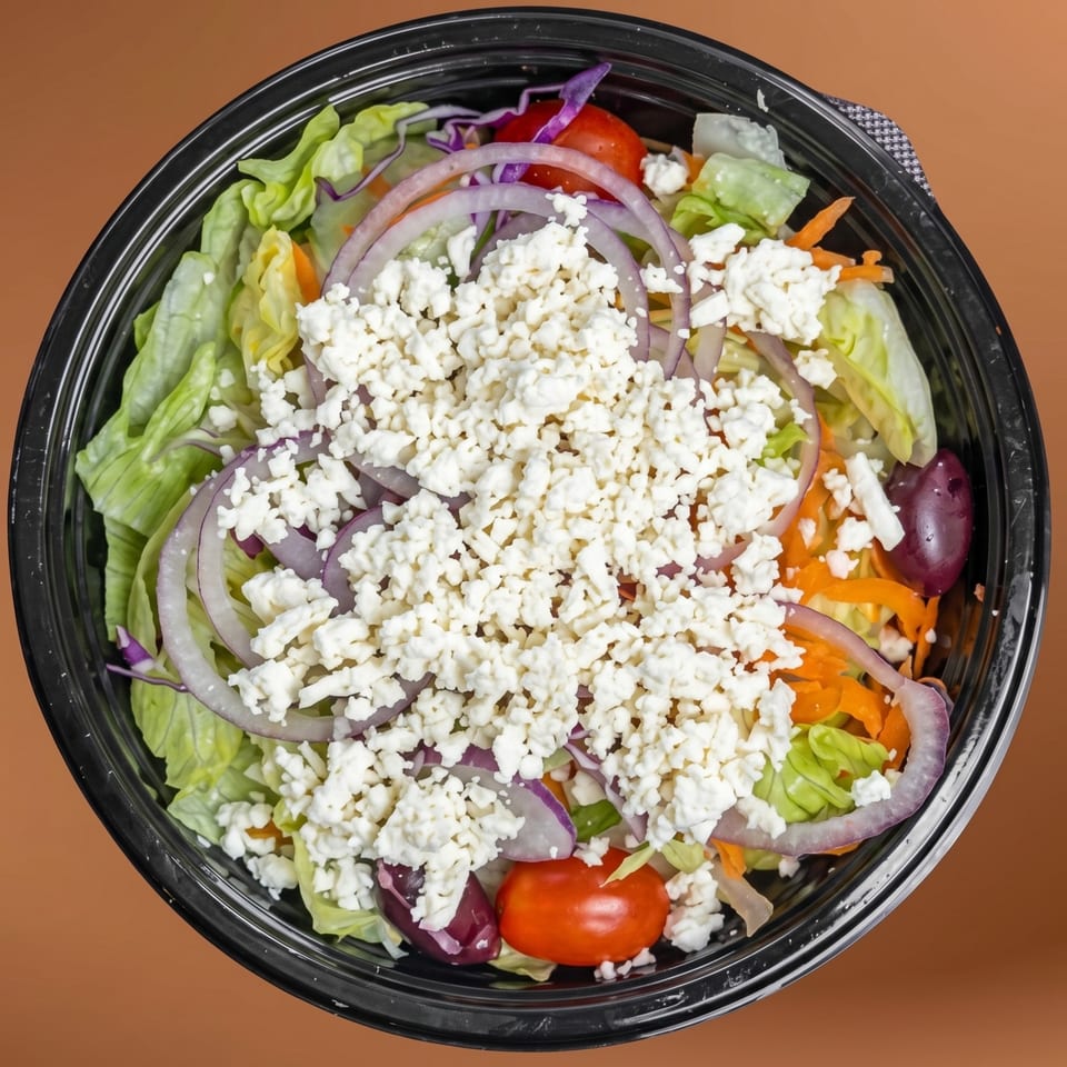 Overhead view of a fresh Greek salad with lettuce, red onions, tomatoes, olives, and feta cheese.