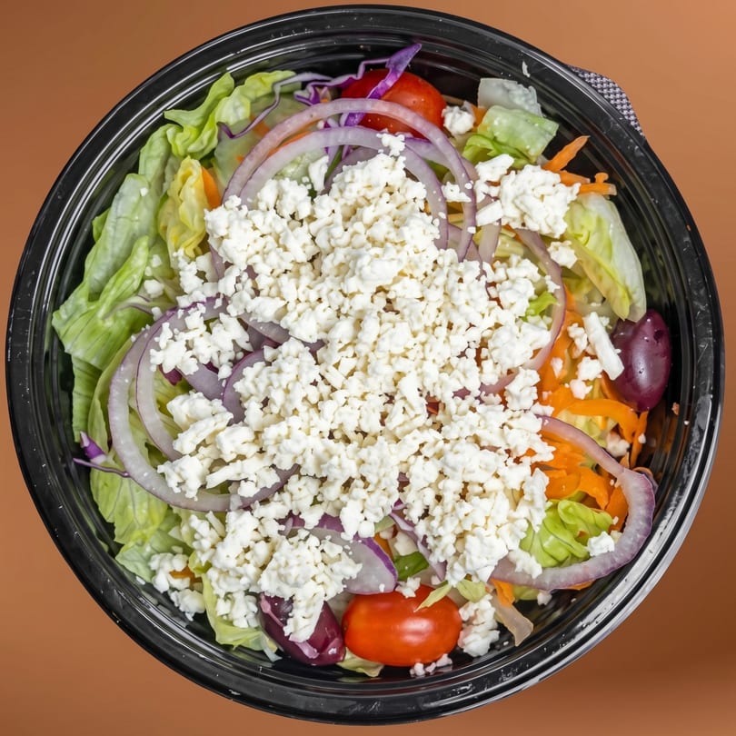 Overhead view of a fresh Greek salad with lettuce, red onions, tomatoes, olives, and feta cheese.